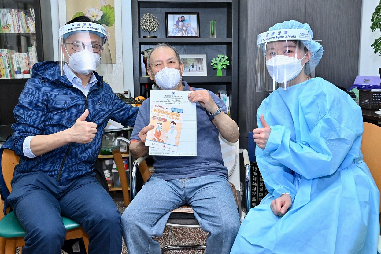 聶德權(左)今日到新翠邨新傑樓，與一名剛接受上門接種新冠疫苗服務的約80歲長者(中)合照。(政府新聞處)