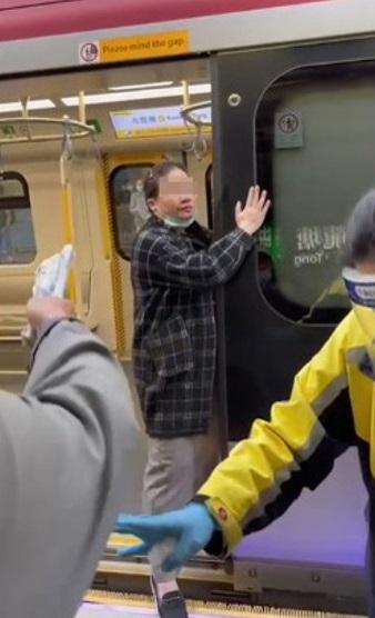 除罩的中年婦站在港鐵列車門口,不斷把口水鼻涕抹在車門周圍,並舉中指指向現場其他乘客。(網片截圖)