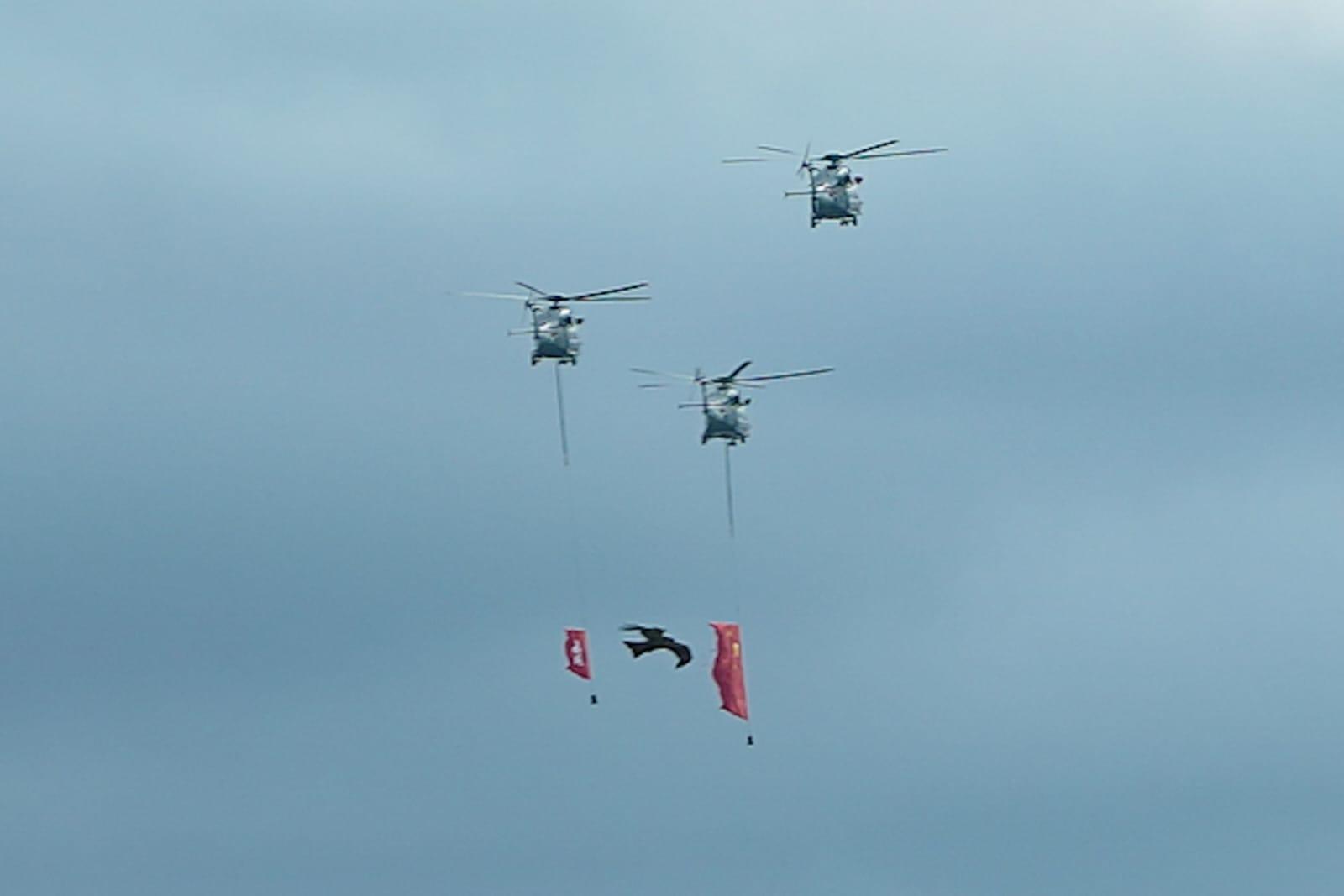 飛行服務隊直升機懸掛著國旗和區旗在上空飛過。(李睿哲攝)