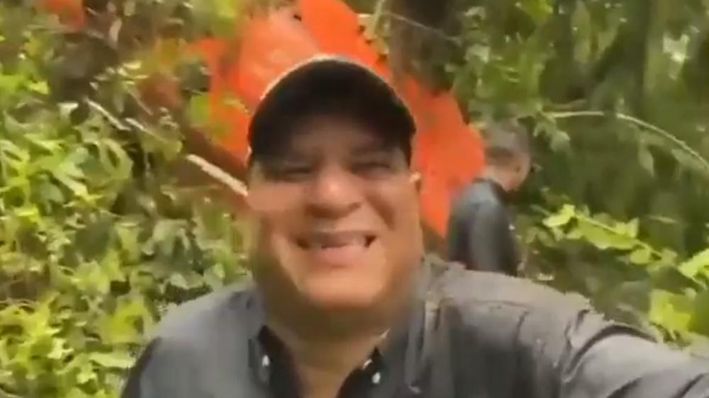 橙色的直升機殘骸就在Dimitri Flores背後的樹叢。(Twitter)