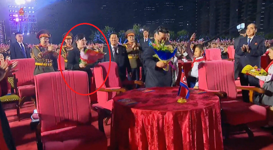 神秘女子在一場戶外音樂會上,拿著花束站在金正恩身後。(互聯網)