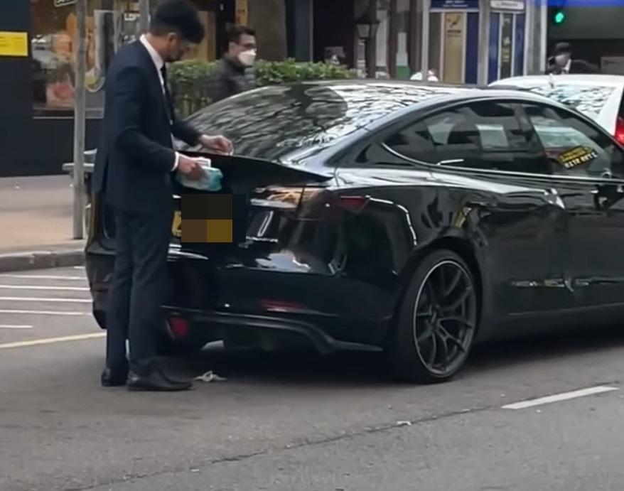 西裝男用濕紙布抹Tesla,再將紙巾踢入車底。(網片截圖)