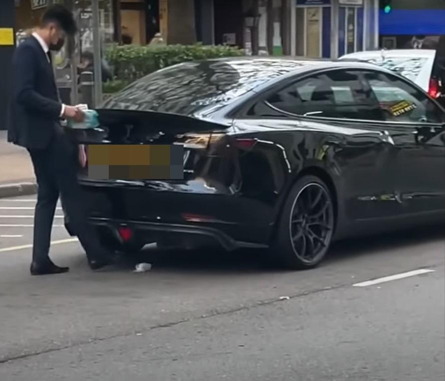 西裝男用濕紙布抹Tesla,再將紙巾踢入車底。(網片截圖)
