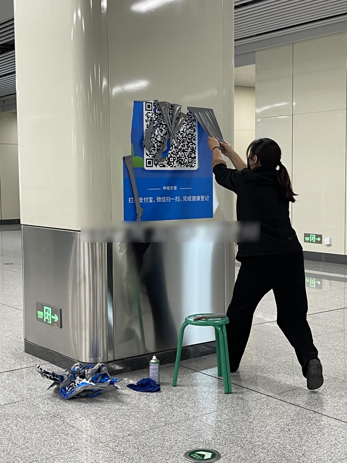 河南鄭州地鐵工作人員清除健康碼掃碼海報。(大河報)