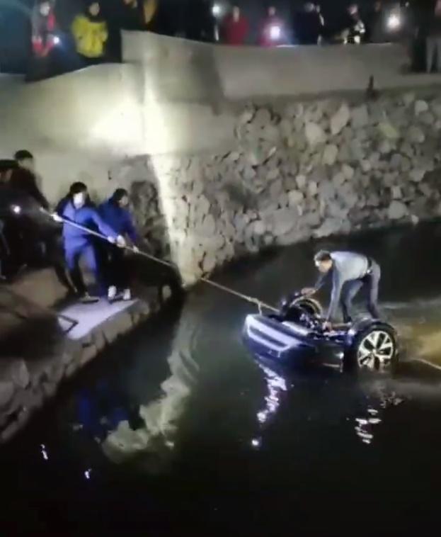 水塘裡的失事車輛僅部分露出水面,有人站上方指揮塘邊人群以大纜繩將車拉回岸邊,塘邊有大批居民圍觀。(微博)