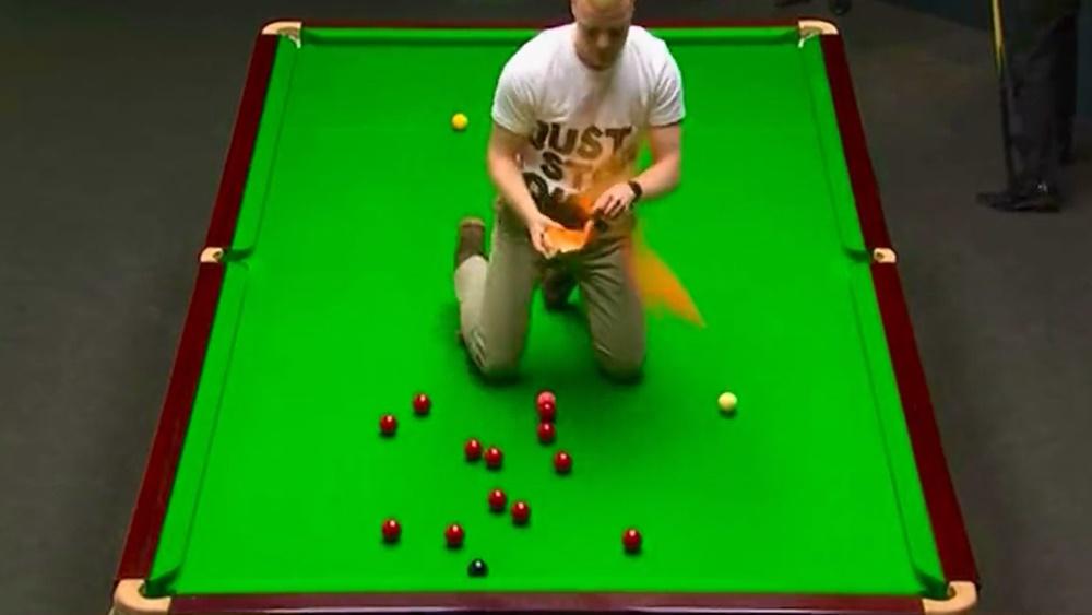 環保組織男成員突然闖入並跪在桌球枱上向灑上橙色粉末,令比賽一度暫停。(Twitter)