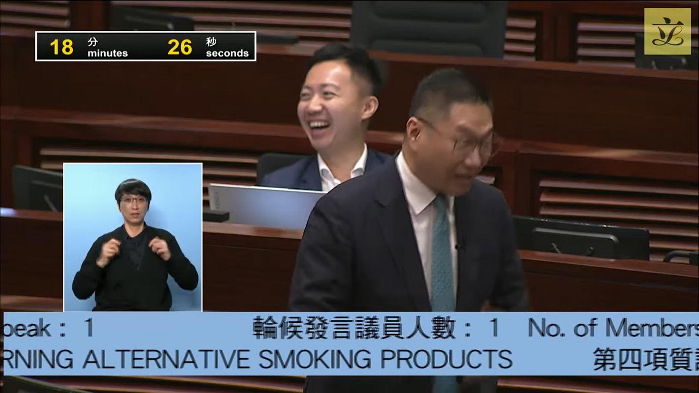 當邵家輝(前)質疑控煙酒辦的「放蛇」形式時,李梓敬(後)笑得合不攏嘴。(立法會直播截圖)