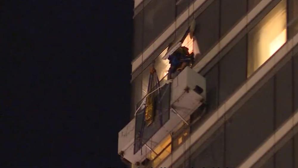消防員接報到場打開樓上單位氣窗,游繩到吊船,將兩人救到安全位置。(電視截圖)
