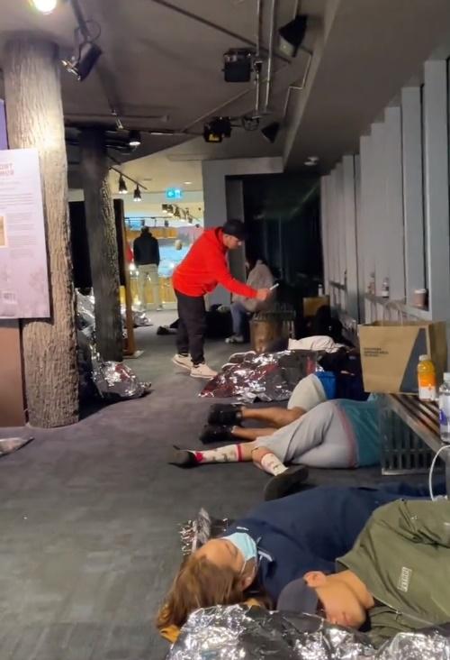 多名遊客蜷縮在應急用的銀色氈子內、睡在地板上過夜。(X)