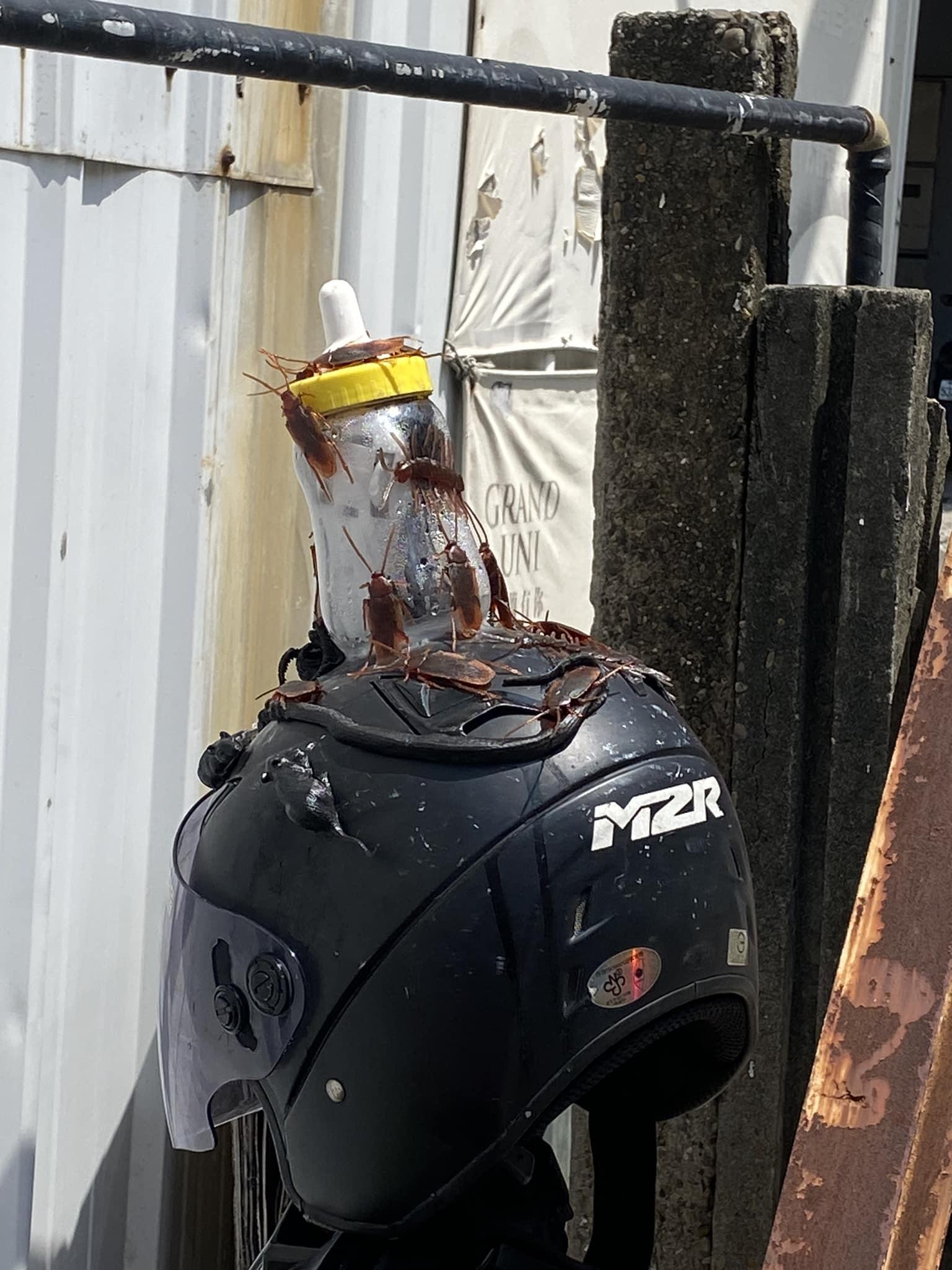 電單車上掛著一頂頭盔,頭盔頂黏著一個佈滿「曱甴」的奶樽。(FB)