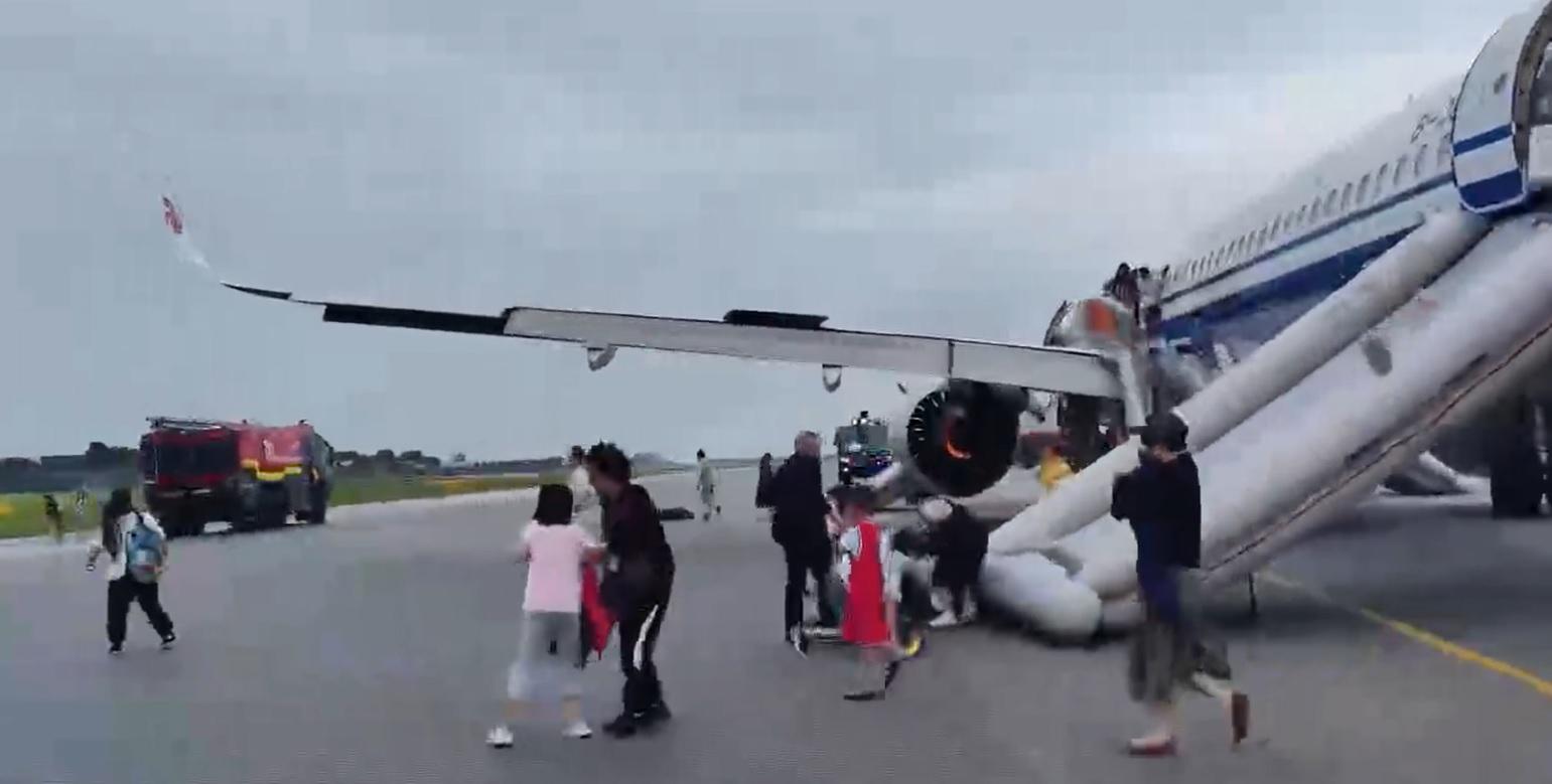 乘客從逃生梯疏散到跑道,客機引擎仍在冒出火焰。(互聯網)