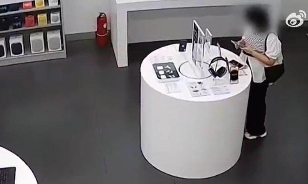 婦人再次接近展示櫃拿起展示的iPhone 14 Plus。(微博)