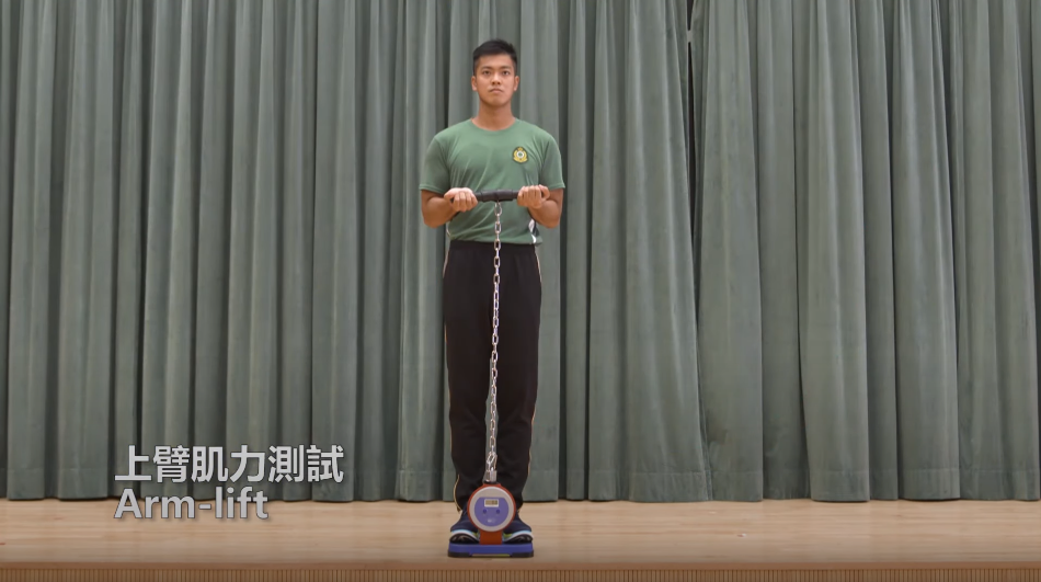海關督察及關員體能測試 臂肌力測試須考生雙腳站上儀器與肩膊同寬,挺胸收緊腰部。上臂微靠身體兩側,雙手反握儀器,集中二頭肌的力量,吸氣並開始彎曲手臂向上拉。(海關截圖)