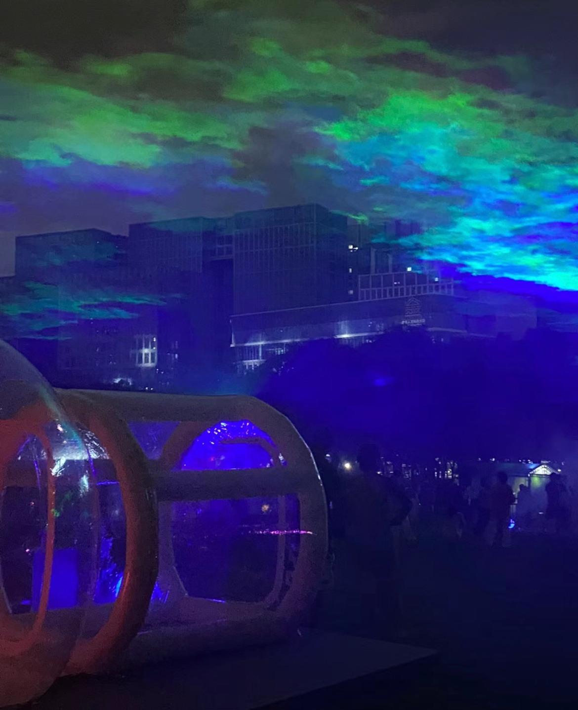 在龍崗大運公園內,「北極」光束在城市高樓大廈上空營造了夢幻的效果。(圖片來源:北山@小紅書)