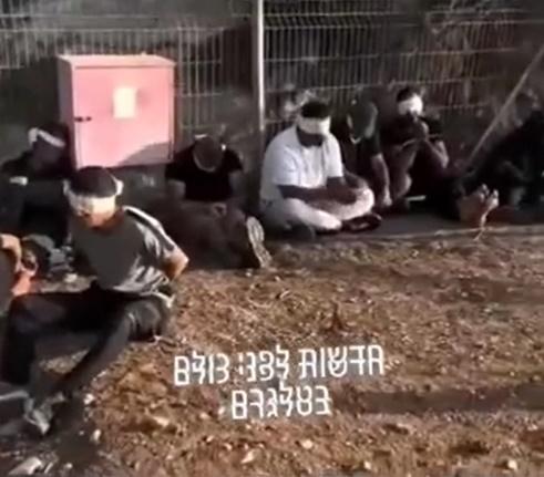 多名被捕的哈馬斯俘虜被白布蒙眼、雙手被綁,靠著鐵柵欄席地而坐,片背景播放著動感十足的音樂。(X)