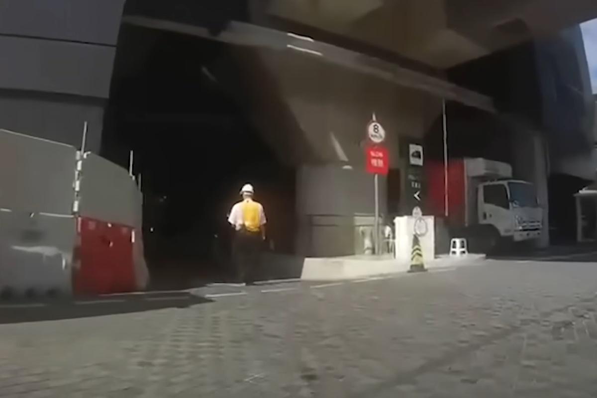 一名身穿反光衣、頭戴安全帽的工人,在圍方停車場入口車路上步行,未見他有留意交通情況。(網上片段截圖)