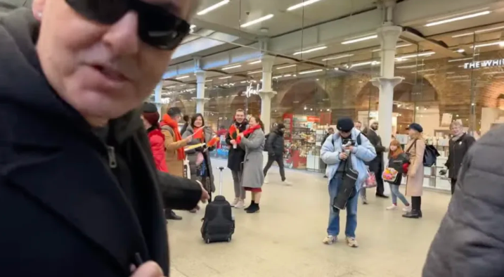 英國鋼琴家「K博士」卡瓦納(Brendan Kavanagh)上周五(19日)在倫敦St. Pancras火車站的街頭鋼琴進行公眾表演,期間身後不遠處站著數名手持中國國旗的遊客