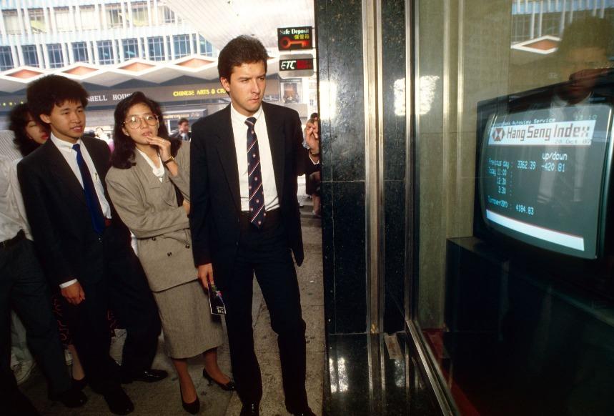 1987年股災的黑色星期一,市民在中環一家銀行門口專注觀看屏幕上的財經資訊。1987年股災期間,香港股市更史無前例停市4日。(圖片來源:Getty)