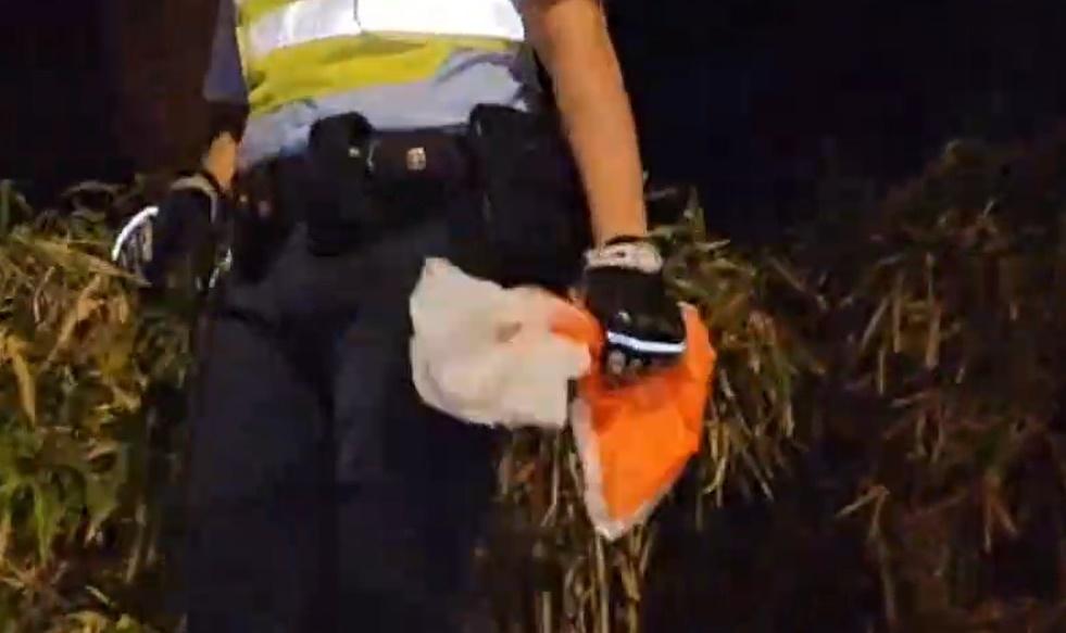 警方到場沿山坡向上搜索後,發現一個載有枇杷膏及單據的橙白色膠袋。(電視截圖)