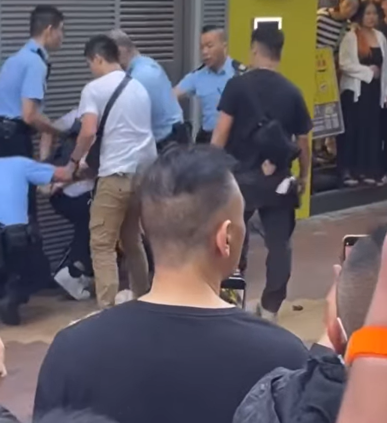 一名街頭歌手周日(24日)下午約4時在旺角朗豪坊對開演唱時,被多名警員包圍制服。(影片截圖)