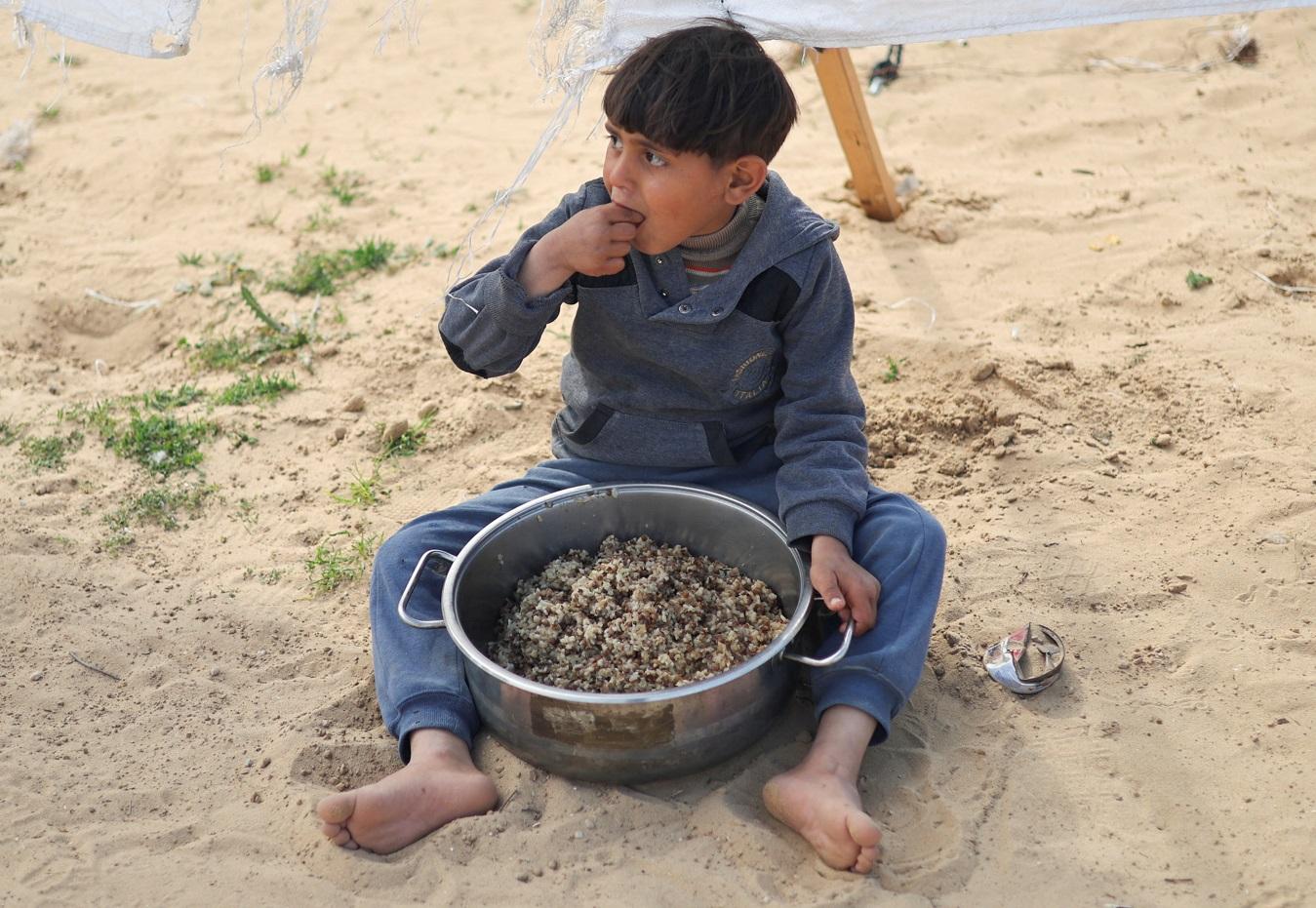 加沙南部拉法難民營兒童就地吃剛領到的糧食。(路透社)