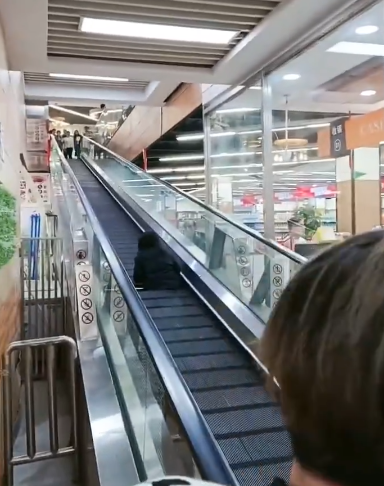 監視畫面顯示事主由自動扶梯上樓購物,涉事扶梯有一塊踏板「離奇消失」,她不幸地正好「踩空」,腿部隨即被捲入,電梯還繼續運行,有男職員見狀按下緊急煞停鈕,此時,女子腰部以下已被捲進扶梯。(影片截圖)