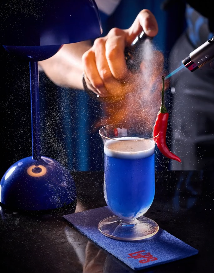 Spicy Blue是火焰雞尾酒,由天然藍色螺旋藻製成,藍色螺旋藻帶很高營養含量,富含蛋白質、礦物質及鐵含量,有助增強免疫系統、新陳代謝及改善消化系統;加入Belvedere 伏特加、泰國紅椒、新鮮青檸、椰子、雲尼拿及少許蛋白,作品口感如絲般柔滑。