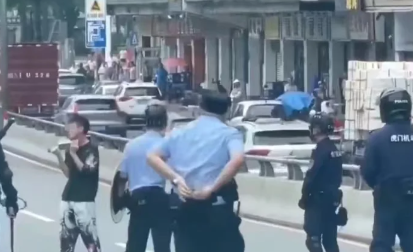 廣東東莞一名涉嫌持菜刀搶劫的男子,在虎門鎮虎門大道路中央手持菜刀架在自己的頸前方,與現場全副武裝的警方對峙,他最終被制服逮捕。(影片截圖)