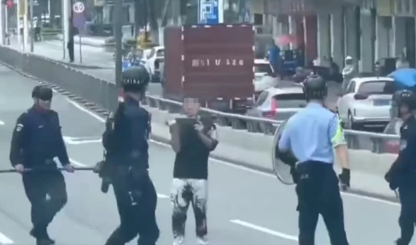 廣東東莞一名涉嫌持菜刀搶劫的男子,在虎門鎮虎門大道路中央手持菜刀架在自己的頸前方,與現場全副武裝的警方對峙,他最終被制服逮捕。(影片截圖)