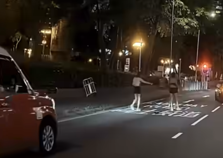 該段影片時長20秒,見到一輛的士在告士打道維多利亞公園對出往高士威道的慢線打「死火燈」,車前有兩名分別穿黑、白色tube top的性感打扮女子,與疑為的士司機的男子因故在路中發生衝突。 FB「車camL(香港群組)」影片截圖