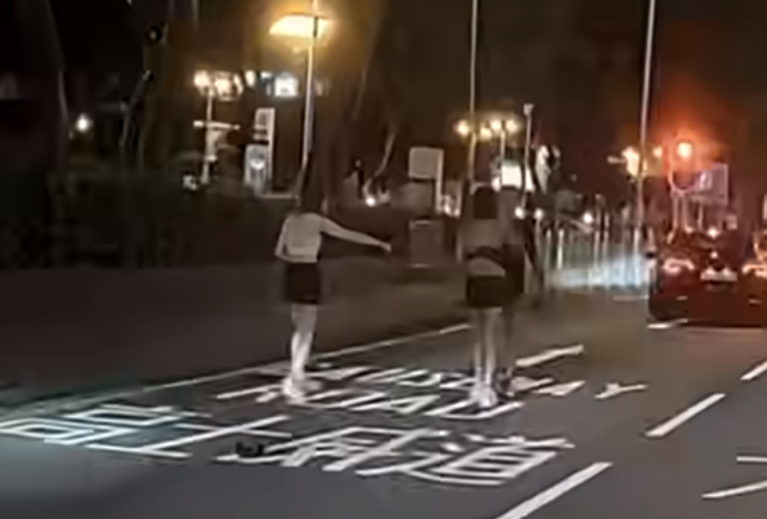 該段影片時長20秒,見到一輛的士在告士打道維多利亞公園對出往高士威道的慢線打「死火燈」,車前有兩名分別穿黑、白色tube top的性感打扮女子,與疑為的士司機的男子因故在路中發生衝突。 FB「車camL(香港群組)」影片截圖