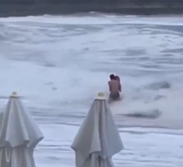 大浪連番湧至打在2人身上,男子隨即護著女友。(X)