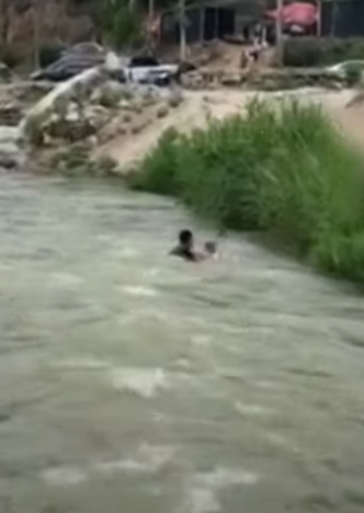 河北保定一名男孩於河邊滑倒被激流捲走,橋上一名大叔奮不顧身跳入水中,以「攔網式」將男孩救起。(影片截圖)