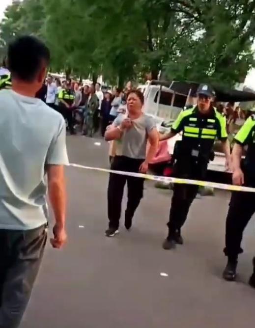 一名身穿淺色上衣男子坐在地上,一名婦人由警員帶走,許多民眾在場圍觀。(微博)