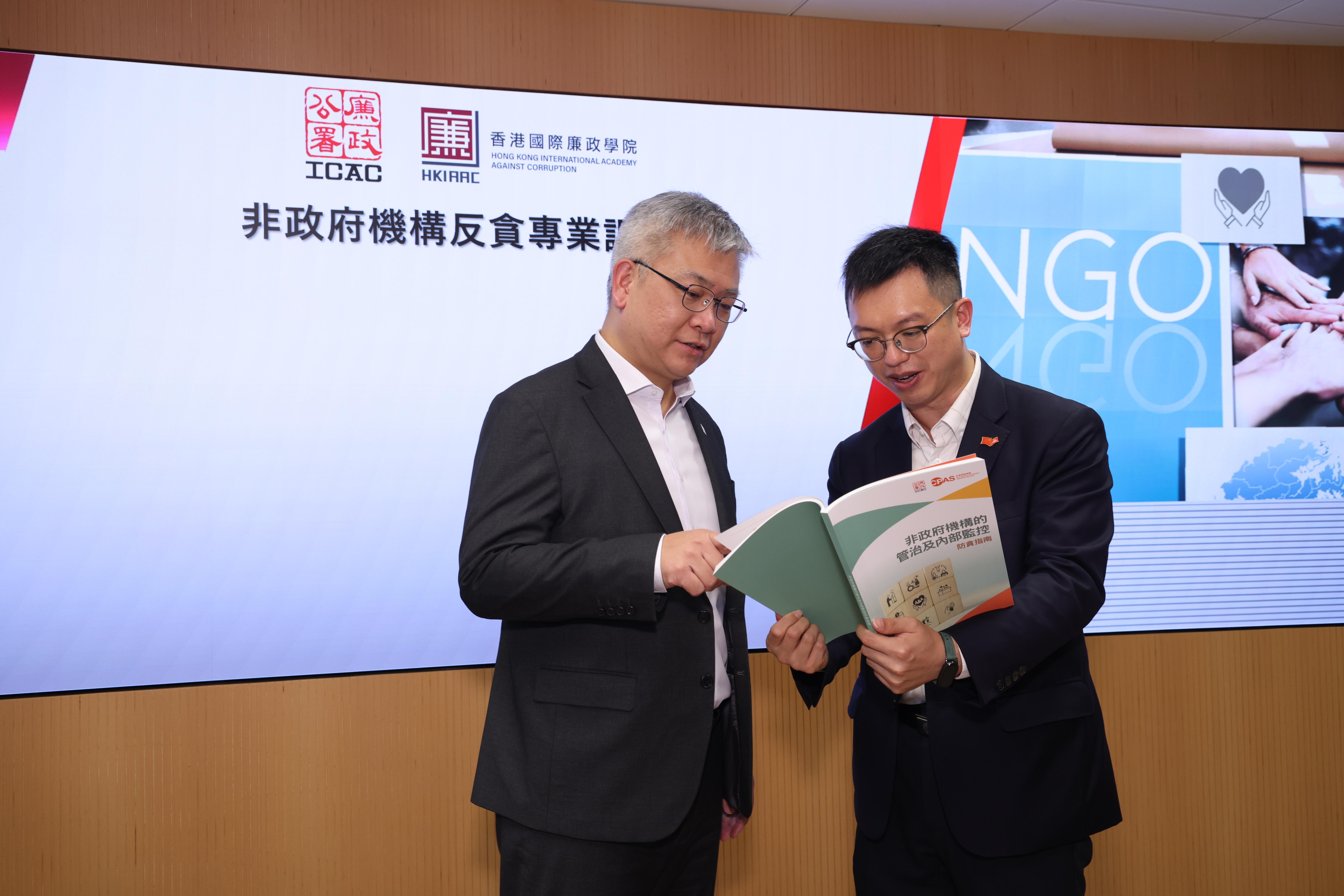 莊家樂向何啟明(右)介紹最新版的《非政府機構的管治及內部監控防貪指南》。