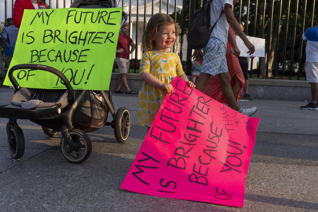 一名兩歲女童與家人在白宮外舉牌表示支持拜登。(美聯社)