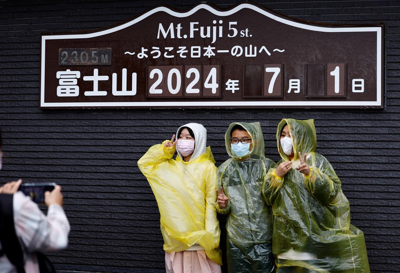 民眾在富士山五合目的標誌前冒雨打卡。(路透社)