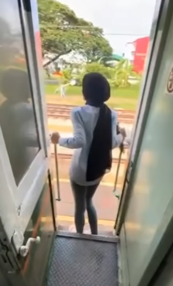 該名女子在火車行駛期間站在敞開的車門梯級,雙手扶住欄杆身體向後傾,及後頭部撞到車外一條柱,她一度失平衡但仍緊握扶手。(影片截圖)