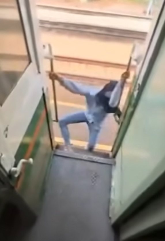 該名女子在火車行駛期間站在敞開的車門梯級,雙手扶住欄杆身體向後傾,及後頭部撞到車外一條柱,她一度失平衡但仍緊握扶手。(影片截圖)
