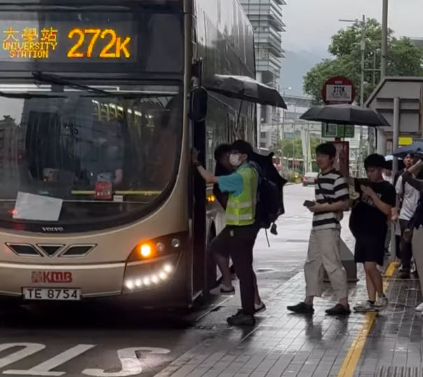 在科學園272K線往大學站的車站,大批乘客正排隊準備上車,該名九巴職員於車門「擔遮」,方便乘客提早收傘上車,亦避免遭淋濕。(社交平台Threads)