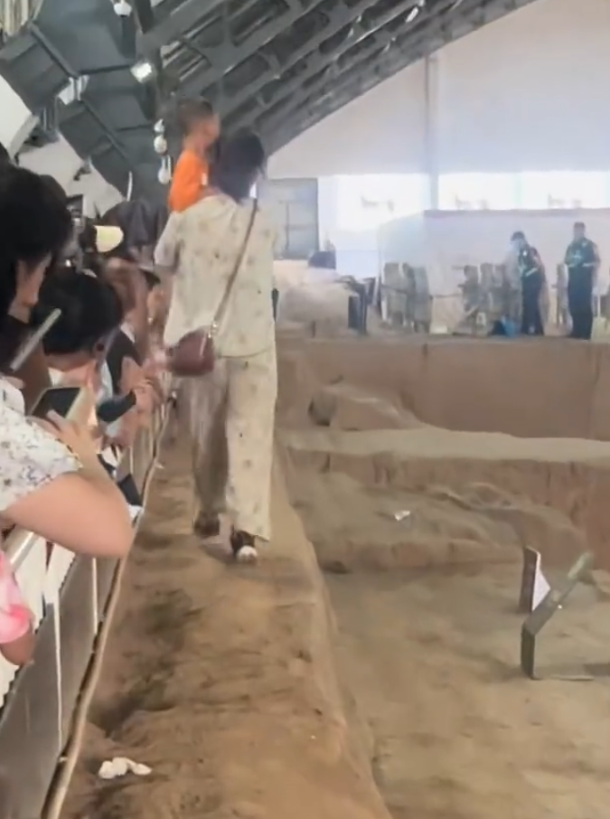 一名母親抱孩子參觀時,突直接跨過護欄走在兵馬俑坑坑道上,最終被保安帶走。(影片截圖)