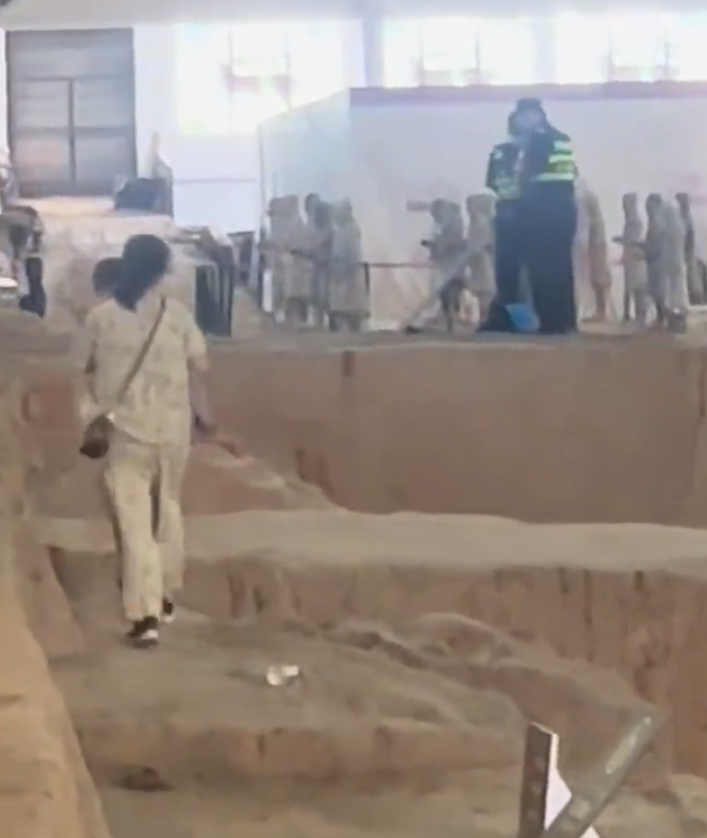 一名母親抱孩子參觀時,突直接跨過護欄走在兵馬俑坑坑道上,最終被保安帶走。(影片截圖)