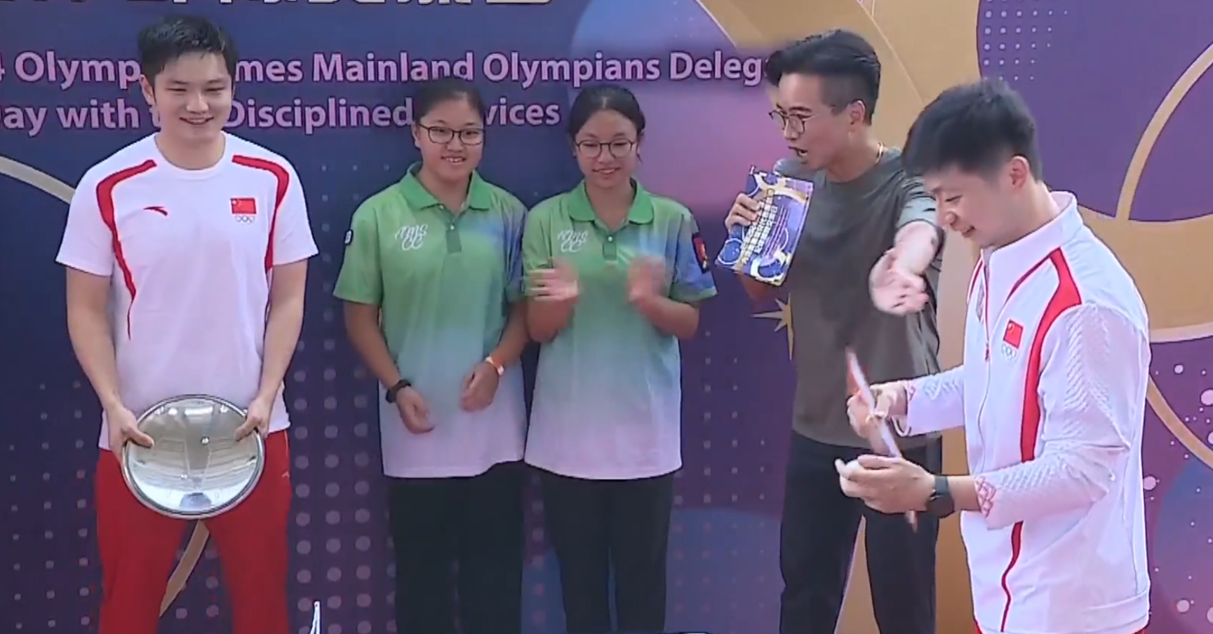 兩名乒乓球選手馬龍、樊振東與青少年較技,為了讓賽,球拍更換成盤子、煲蓋、鑊鏟(電視畫面)