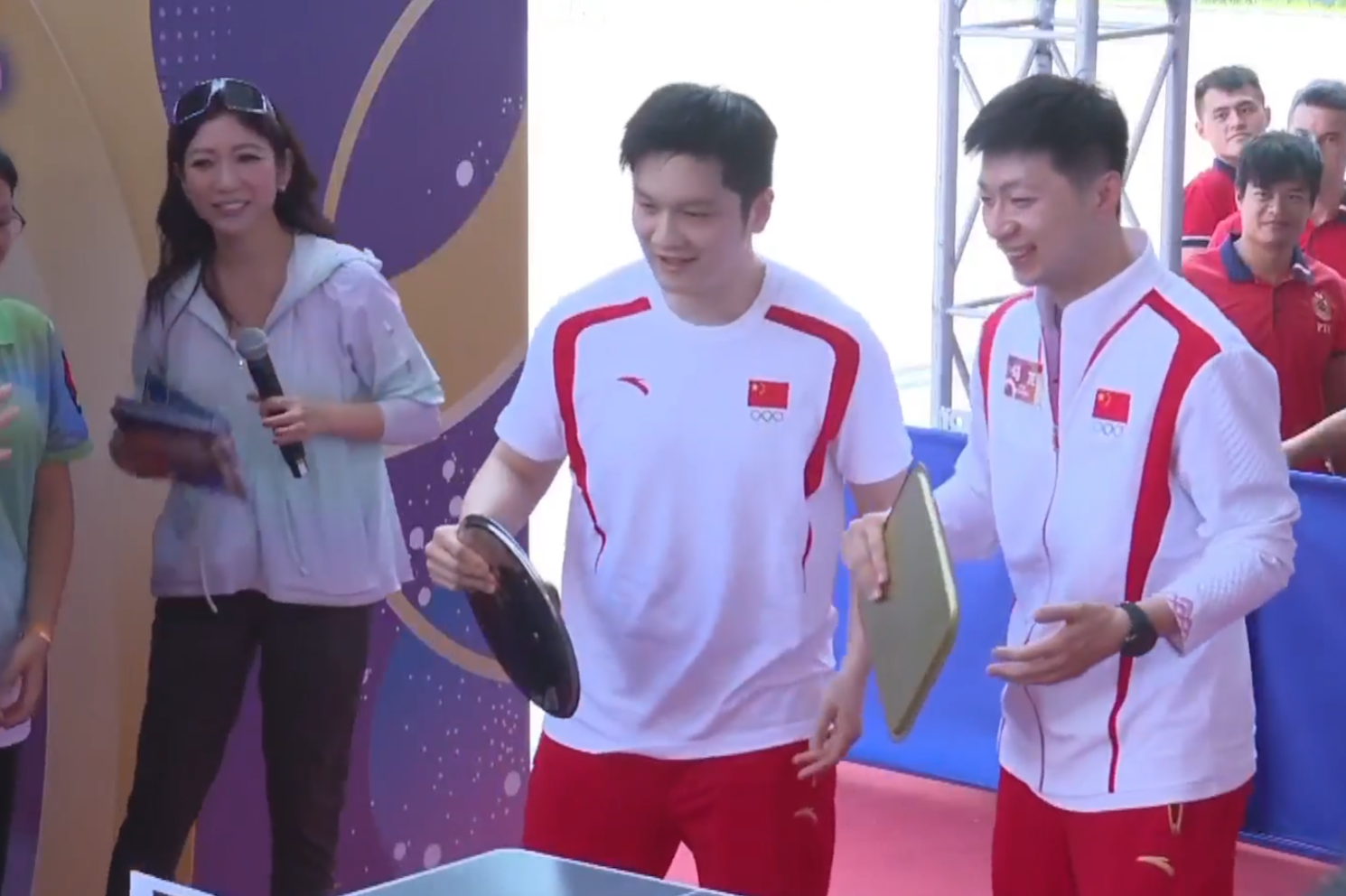 兩名乒乓球選手馬龍、樊振東與青少年較技,為了讓賽,球拍更換成盤子、煲蓋、鑊鏟(電視畫面)