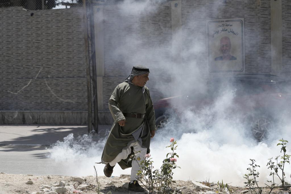 以軍上周六在西岸一個巴勒斯坦難民營施放催淚彈,一名巴人走避。(美聯社)