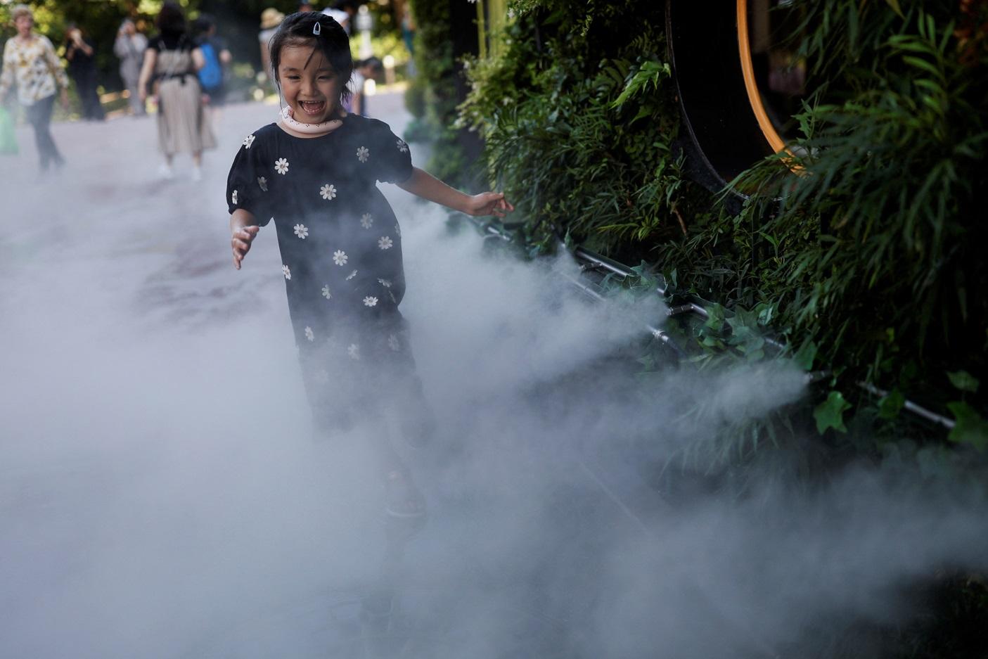東京小女孩走進街頭噴霧中嬉戲消暑。(路透社)
