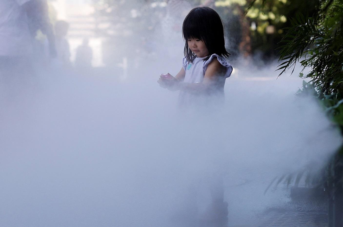 東京小女孩走進街頭噴霧中消暑。(路透社)