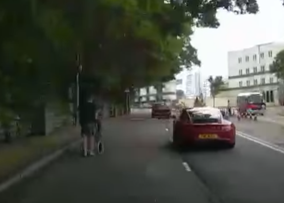 港島薄扶林道近瑪麗醫院路段一名男子推着需坐輪椅的長者於路邊「慢步」,與車輛驚險擦身而過,Cam主發現後即時響咹煞車爆粗,大罵男子行為危險。(影片截圖)
