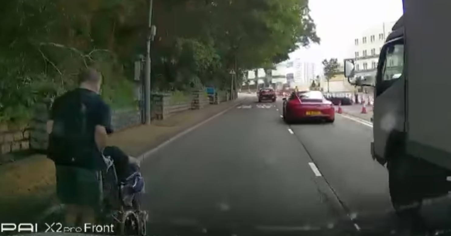 港島薄扶林道近瑪麗醫院路段一名男子推着需坐輪椅的長者於路邊「慢步」,與車輛驚險擦身而過,Cam主發現後即時響咹煞車爆粗,大罵男子行為危險。(影片截圖)