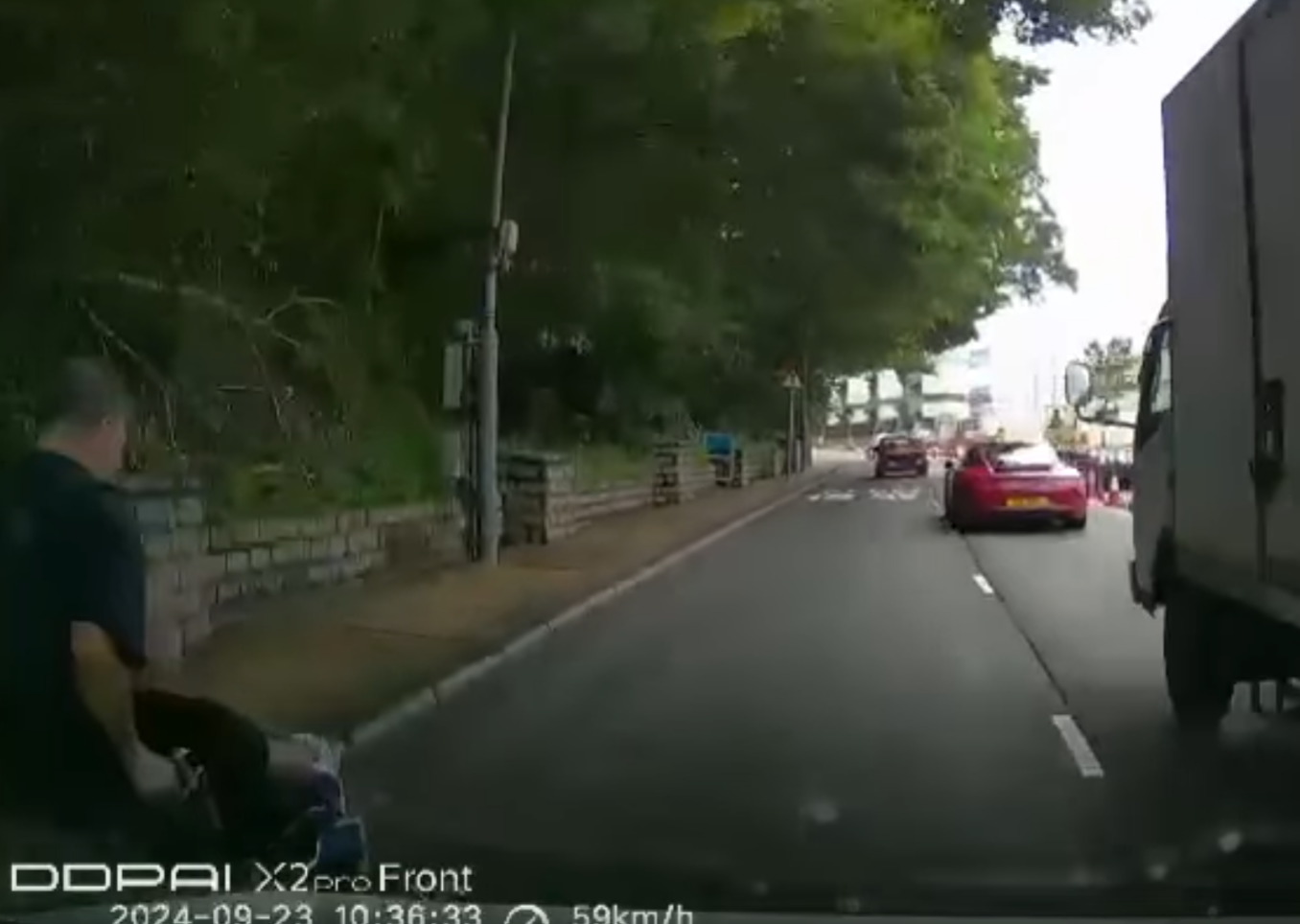 港島薄扶林道近瑪麗醫院路段一名男子推着需坐輪椅的長者於路邊「慢步」,與車輛驚險擦身而過,Cam主發現後即時響咹煞車爆粗,大罵男子行為危險。(影片截圖)